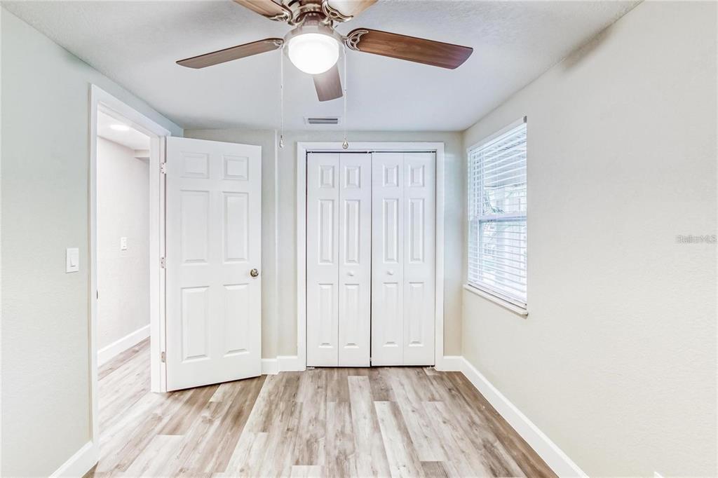 A bedroom with light-colored walls, wood-look flooring, a ceiling fan, and white closet doors — 5320 CHERRY AVENUE, SEFFNER, FL
