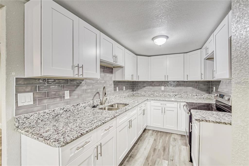 A kitchen with white cabinets, granite countertops, gray subway tile backsplash, and light wood flooring — 5320 CHERRY AVENUE, SEFFNER, FL