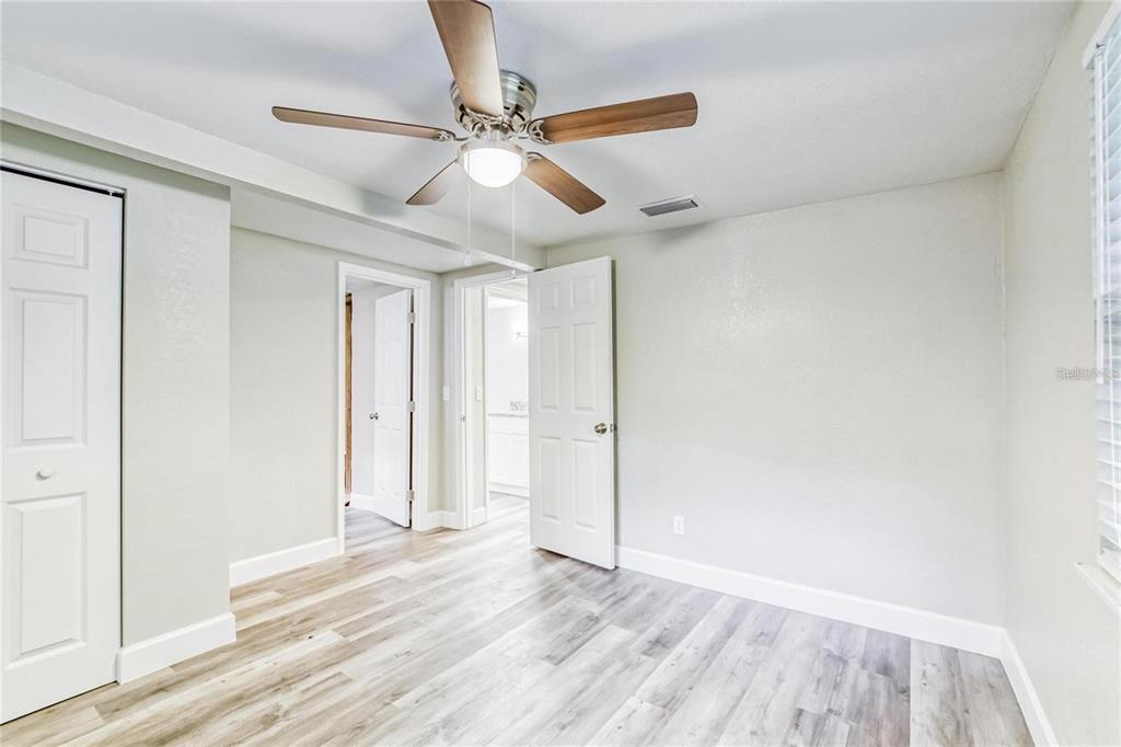 A bedroom with light gray walls, wood-look flooring, a ceiling fan, and two open doors — 5320 CHERRY AVENUE, SEFFNER, FL