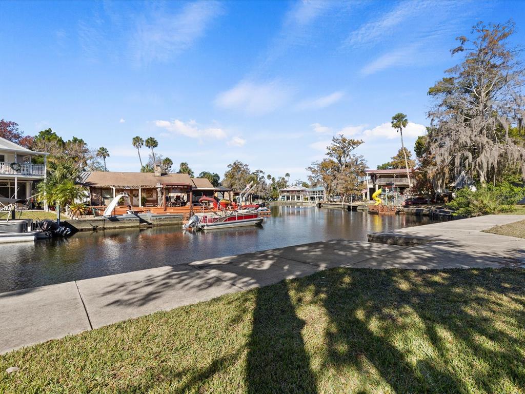 A canal view features several docked pontoon boats and waterfront homes under a blue sky — 7255 TROPICAL DRIVE, WEEKI WACHEE, FL