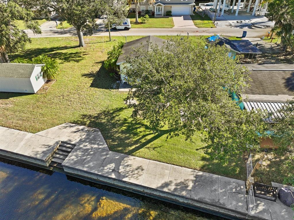 An aerial view shows a house with a large tree, a shed, and a concrete seawall — 7255 TROPICAL DRIVE, WEEKI WACHEE, FL
