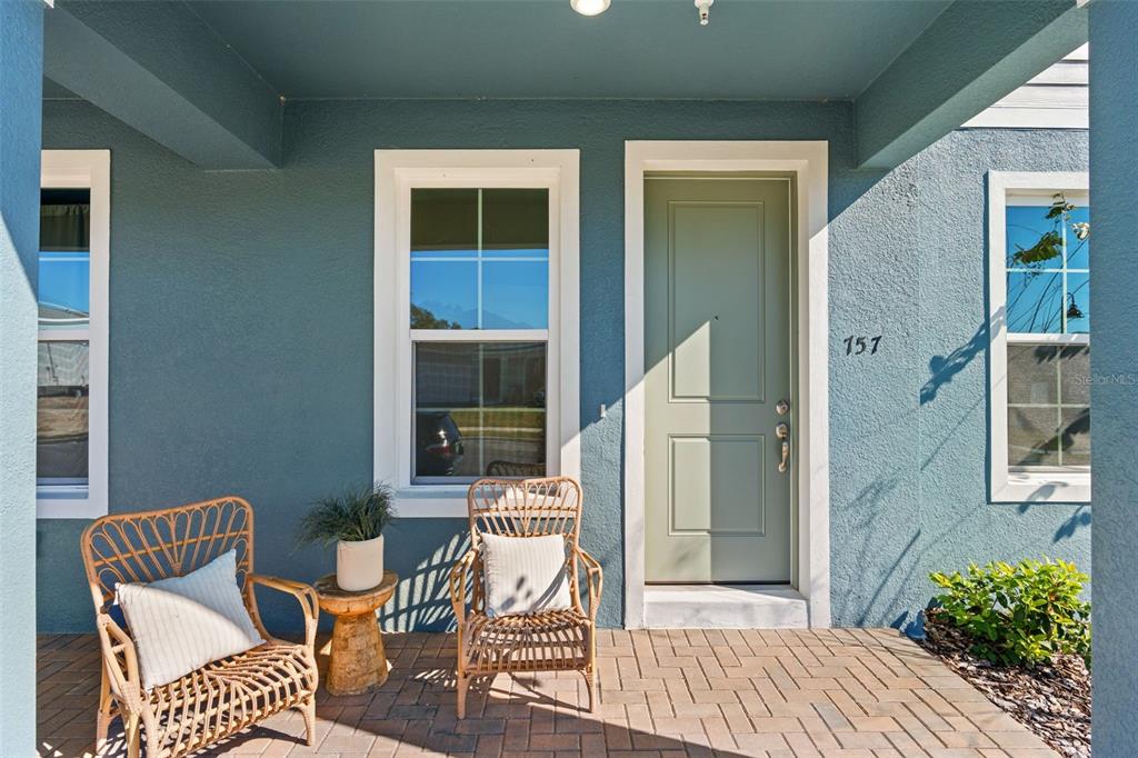 A blue-walled front porch features a sage green door, two wicker chairs, and brick flooring — 672 EMERALD GROVE DRIVE, APOPKA, FL