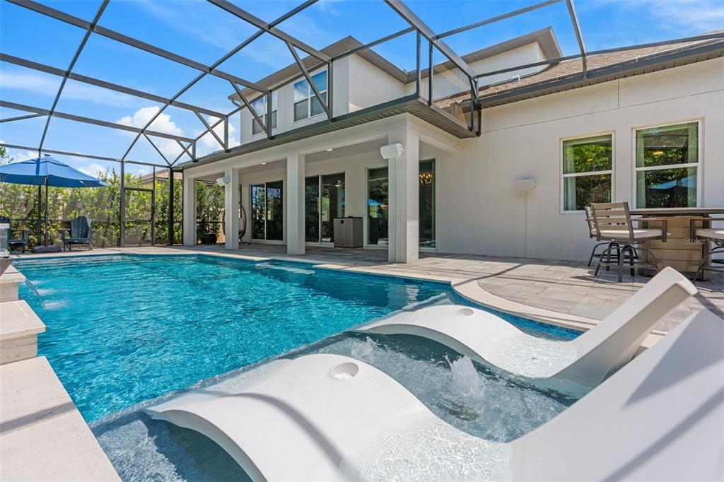A swimming pool with lounge chairs sits under a screened enclosure beside a house patio — 3336 LONE CYPRESS POINT, OVIEDO, FL