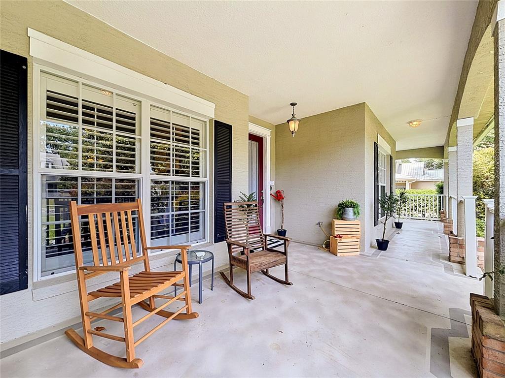 A covered front porch features two wooden rocking chairs, potted plants, and a red door — 19512 SPRING OAK DRIVE, EUSTIS, FL