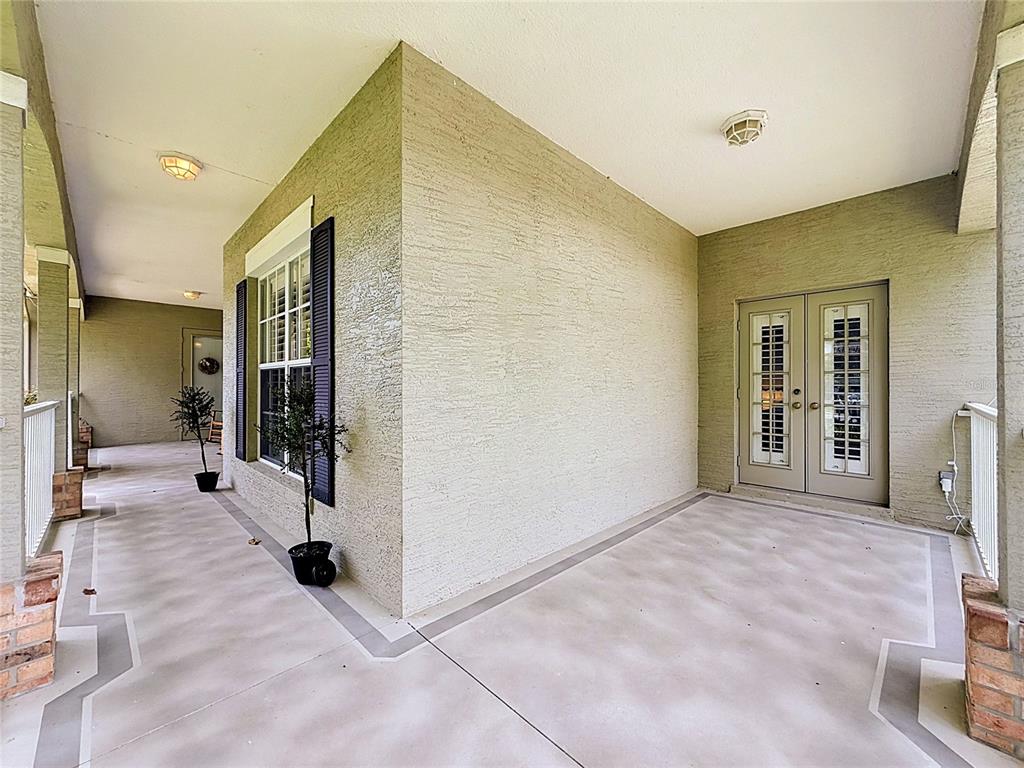 A covered porch features a textured beige wall, double glass doors, and a concrete floor — 19512 SPRING OAK DRIVE, EUSTIS, FL