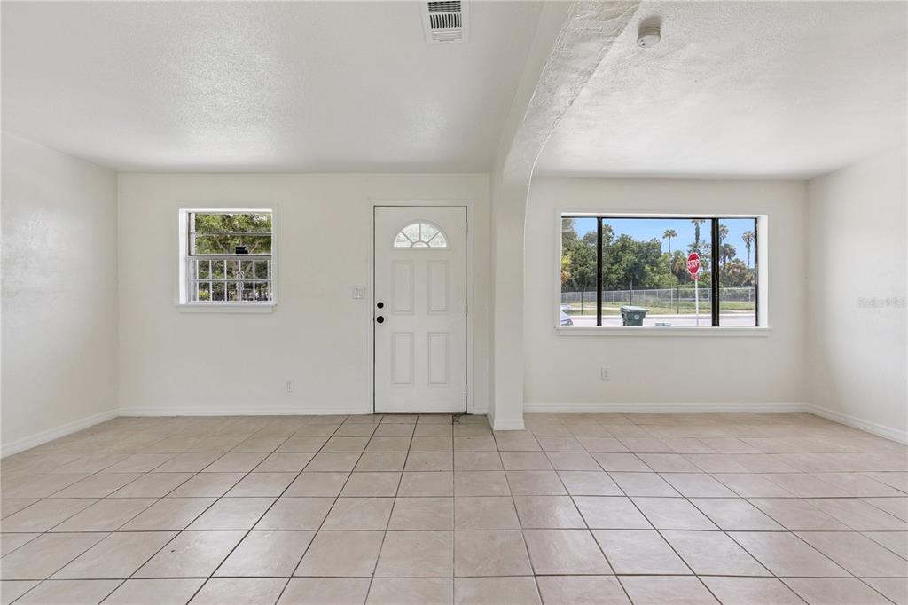 An empty room with white walls, beige tile flooring, a front door, and two windows — 875 LOOMIS AVENUE, DAYTONA BEACH, FL