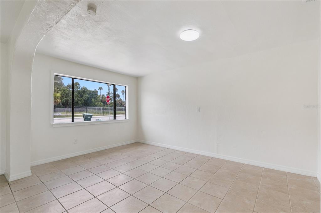 An empty room with white walls, beige tile flooring, and a large window — 875 LOOMIS AVENUE, DAYTONA BEACH, FL