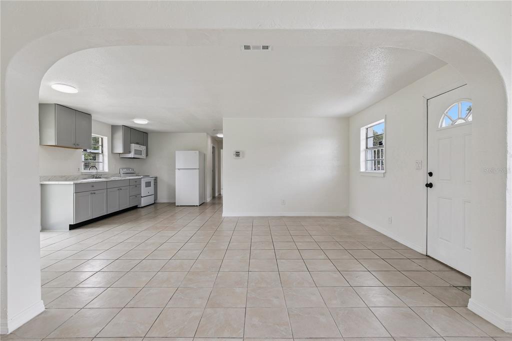 An open-concept kitchen and living area features white walls, tile flooring, and gray cabinetry — 875 LOOMIS AVENUE, DAYTONA BEACH, FL