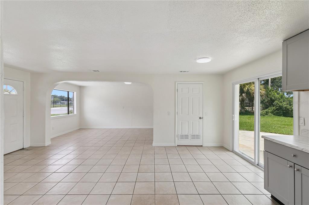 A bright, open-concept room features light tile flooring, white walls, and a sliding glass door — 875 LOOMIS AVENUE, DAYTONA BEACH, FL