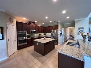 A kitchen features dark wood cabinets, granite countertops, a center island, and stainless steel appliances — 17419 BELLA NOVA DRIVE, ORLANDO, FL