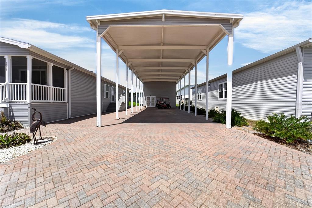 A paved driveway features a large covered carport situated between two light gray mobile homes — 10039 STERLING AVENUE, DADE CITY, FL