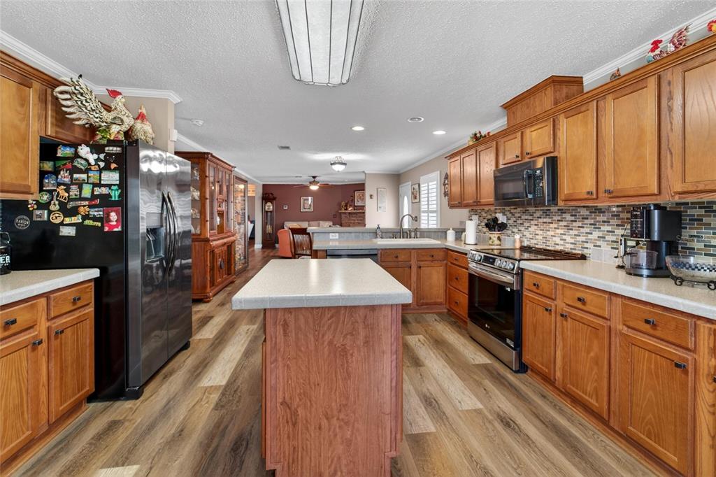 A kitchen features wood cabinets, a central island, stainless steel appliances, and wood-look flooring — 10039 STERLING AVENUE, DADE CITY, FL