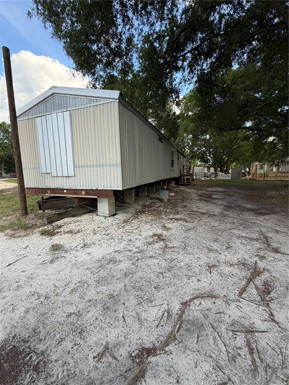 A mobile home with metal siding sits on a sandy lot under large trees — 1059 NE SUGAR BABE ROAD, ARCADIA, FL