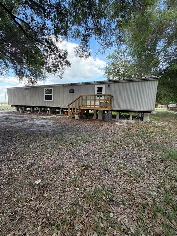 A single-wide mobile home stands on concrete block piers with a wooden deck entrance — 1059 NE SUGAR BABE ROAD, ARCADIA, FL