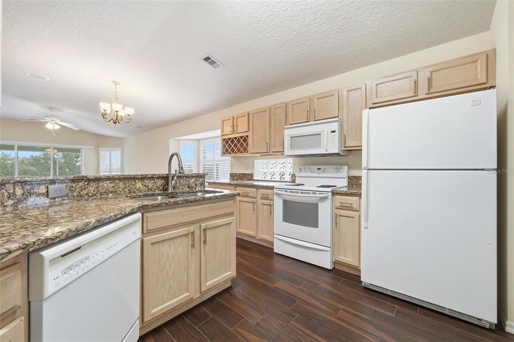 A kitchen features light wood cabinets, granite countertops, white appliances, and dark wood-look flooring — 2311 N ANDREA POINT, LECANTO, FL