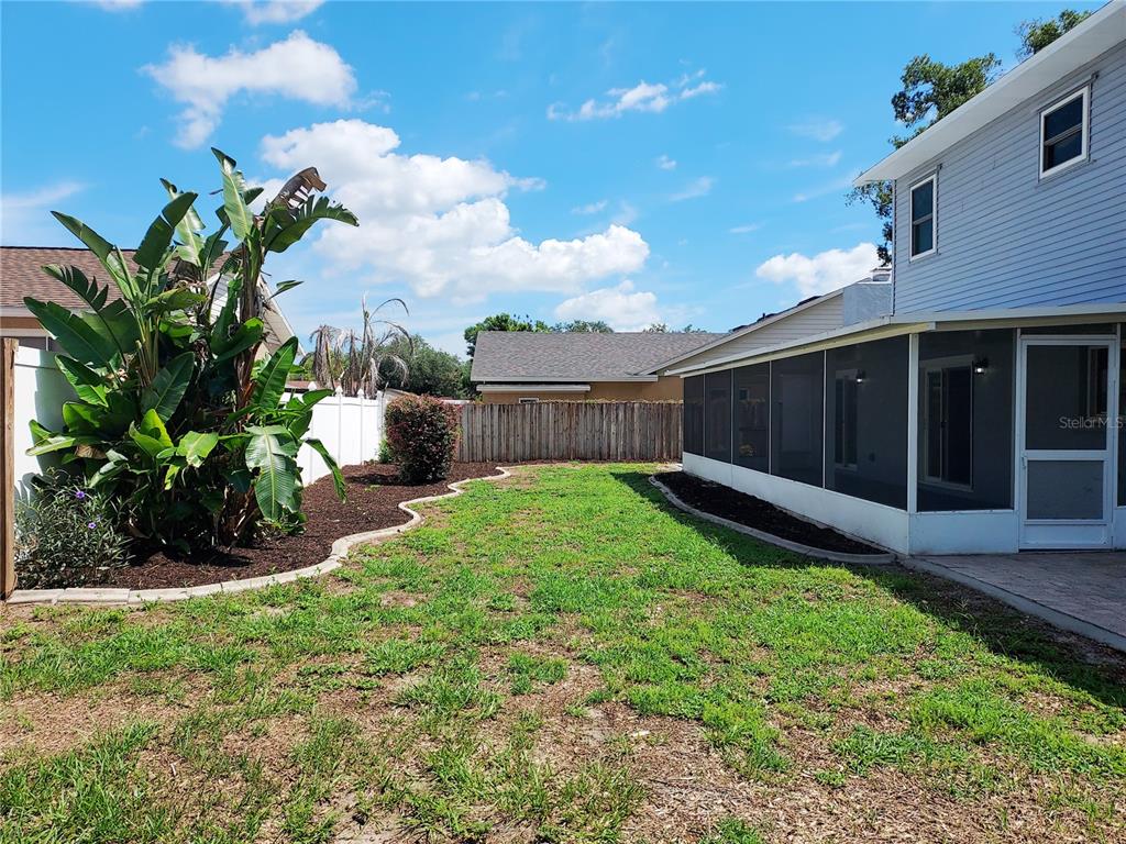 A backyard features a screened-in patio, a large banana plant, and a wooden fence — 702 HYSSOP PLACE, BRANDON, FL