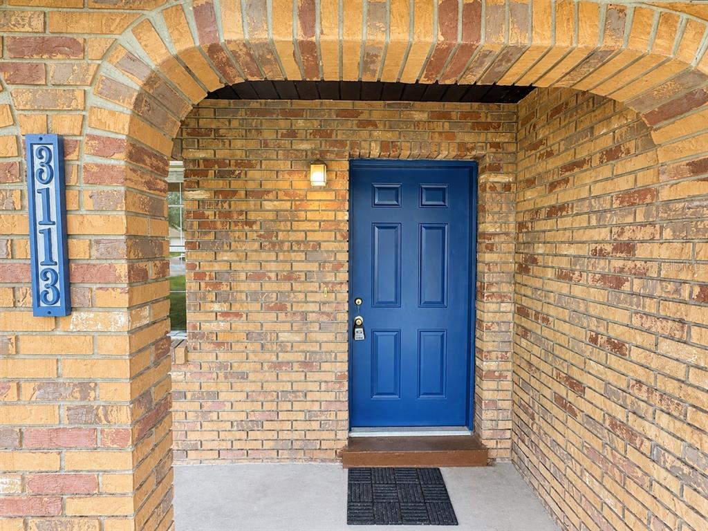 A brick entryway features an arched porch, a blue front door, and a vertical address sign — 3113 WOODHILL ROAD, WINTER HAVEN, FL