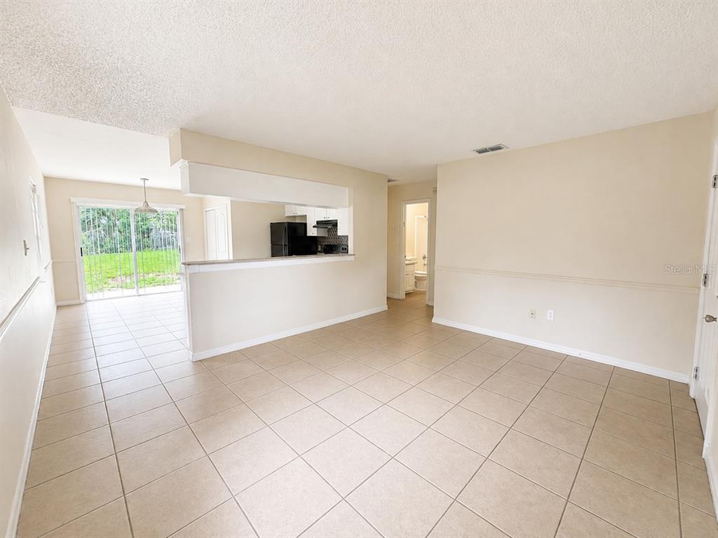 An open-concept living area with beige tile flooring, a kitchen pass-through, and sliding glass doors — 3113 WOODHILL ROAD, WINTER HAVEN, FL