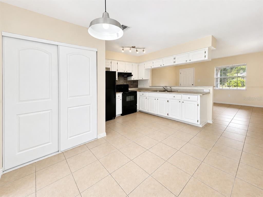 A kitchen with white cabinets, black appliances, and tile flooring opens to a dining area — 3113 WOODHILL ROAD, WINTER HAVEN, FL