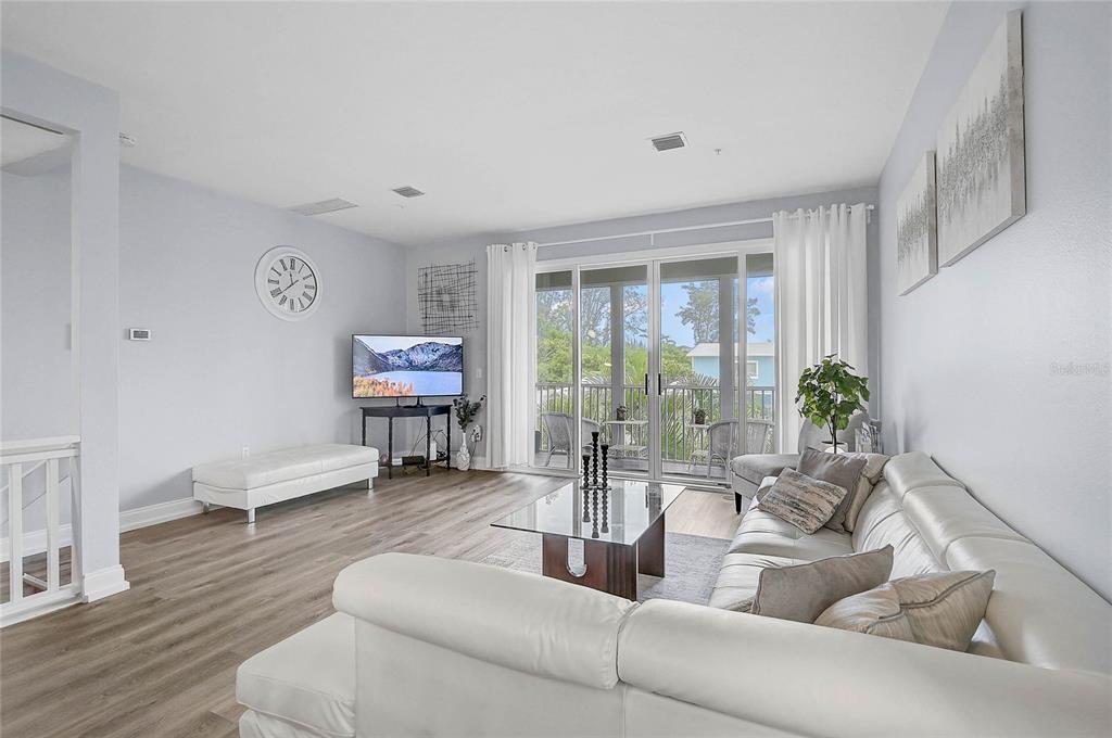 A bright living room features light wood flooring, a white sectional sofa, and sliding glass doors — 508 FOREST WAY, LONGBOAT KEY, FL
