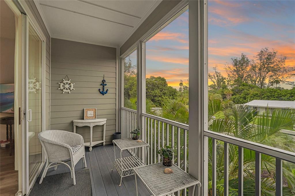 A screened-in balcony features wicker furniture, nautical wall decor, and views of tropical greenery — 508 FOREST WAY, LONGBOAT KEY, FL