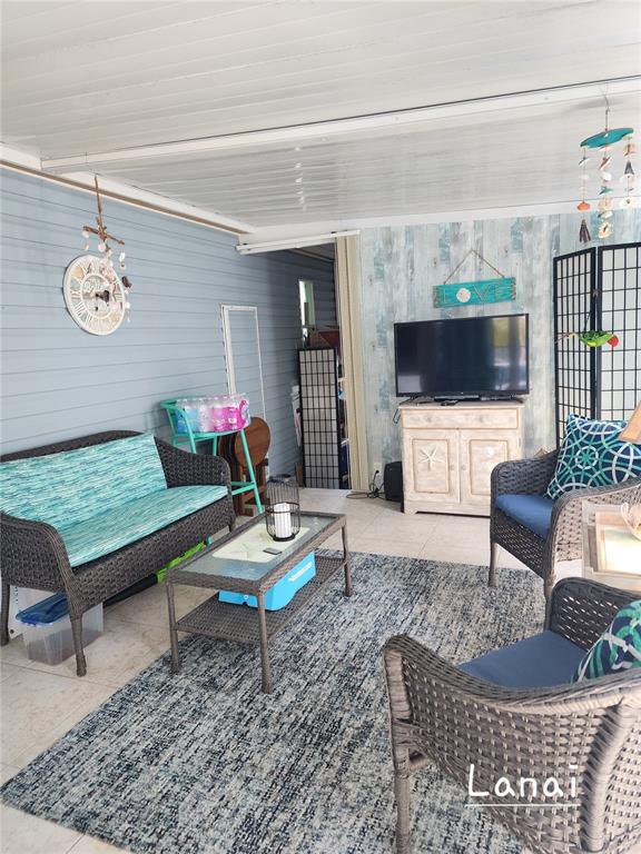 A covered lanai features wicker furniture, a television on a cabinet, and a patterned rug — 1001 STARKEY ROAD UNIT 758, LARGO, FL