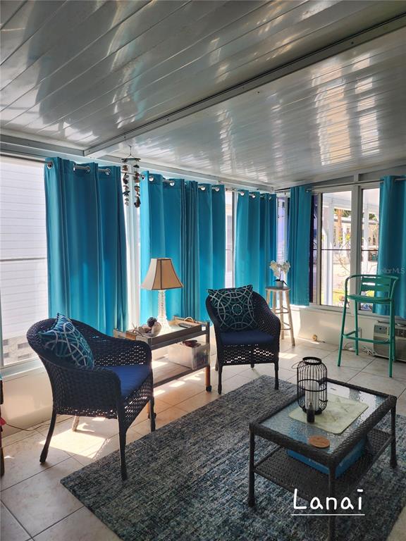 A sunroom features wicker furniture, blue curtains, a glass-topped coffee table, and tiled flooring — 1001 STARKEY ROAD UNIT 758, LARGO, FL