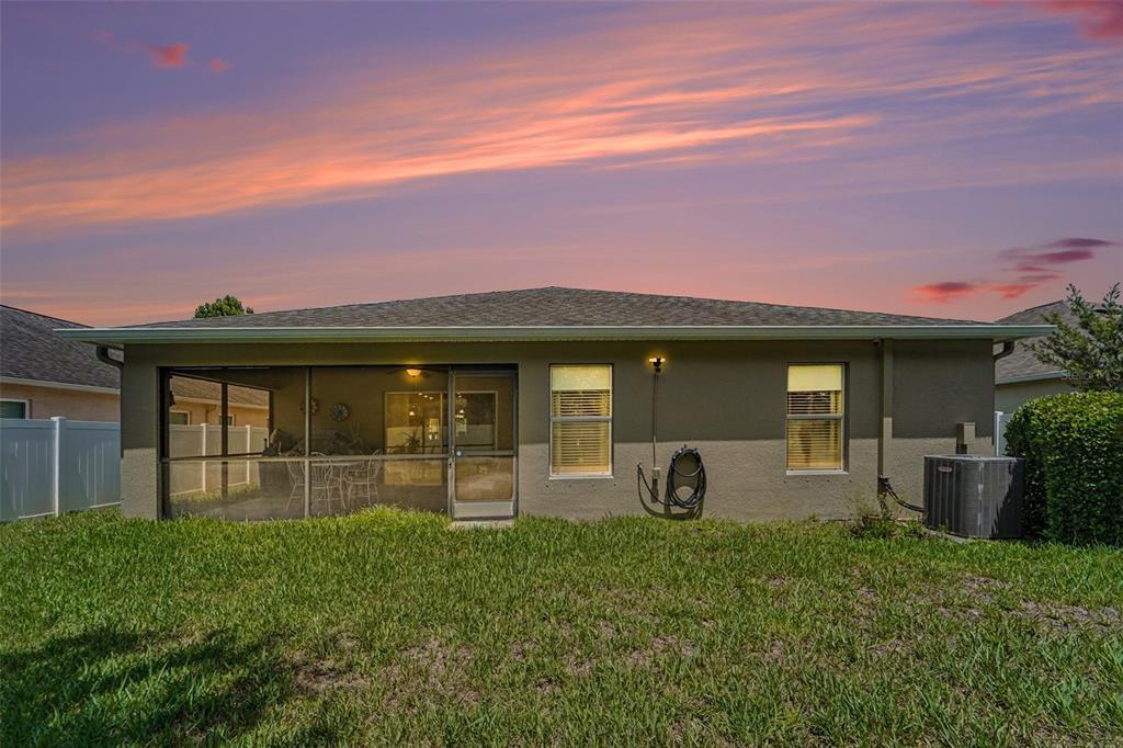 The rear exterior of a house features a screened-in patio, two windows, and a lawn — 10048 IVES LOOP, HUDSON, FL