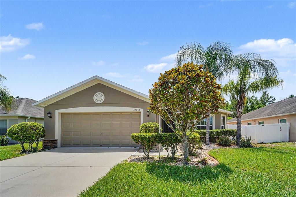 A single-story house with a beige exterior, a two-car garage, and a landscaped front yard — 10048 IVES LOOP, HUDSON, FL