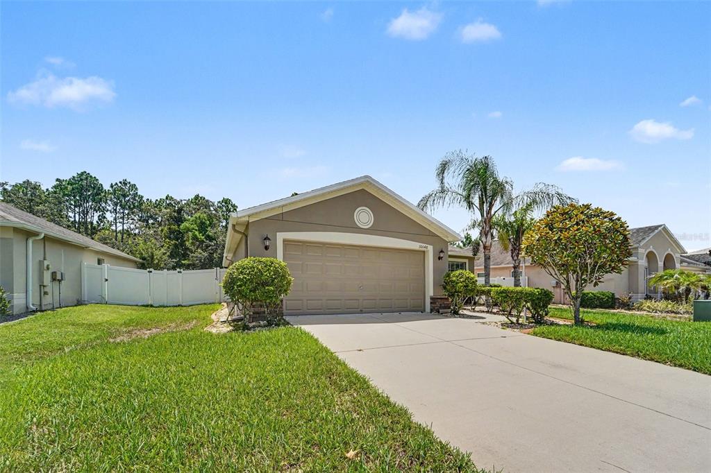 A single-story house with a beige exterior, a two-car garage, and a concrete driveway — 10048 IVES LOOP, HUDSON, FL