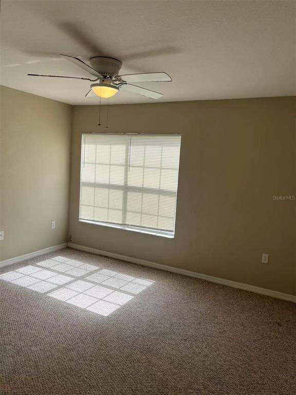 An empty bedroom features beige walls, carpeted flooring, a ceiling fan, and a window with blinds — 10452 WHITE LAKE COURT UNIT 10452, TAMPA, FL