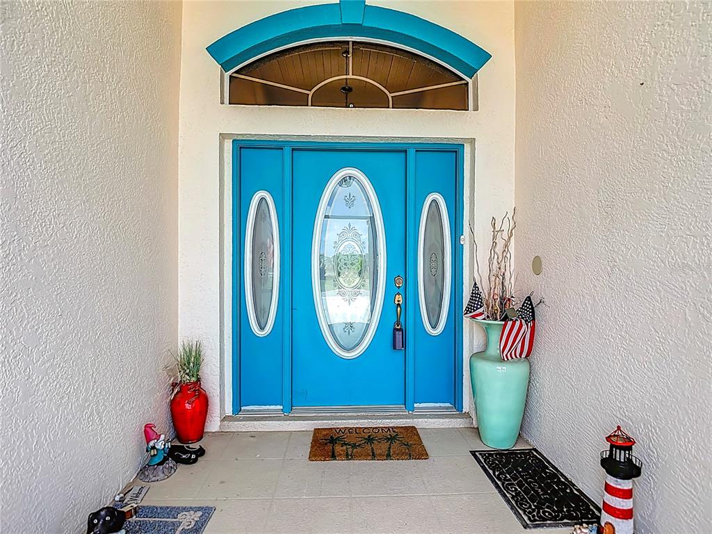 A bright blue front door with glass inserts sits under an arched transom window — 8410 MAYBELLE DRIVE, WEEKI WACHEE, FL