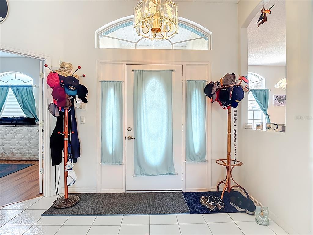 An entryway features a white front door with sidelights, a chandelier, and two coat racks — 8410 MAYBELLE DRIVE, WEEKI WACHEE, FL