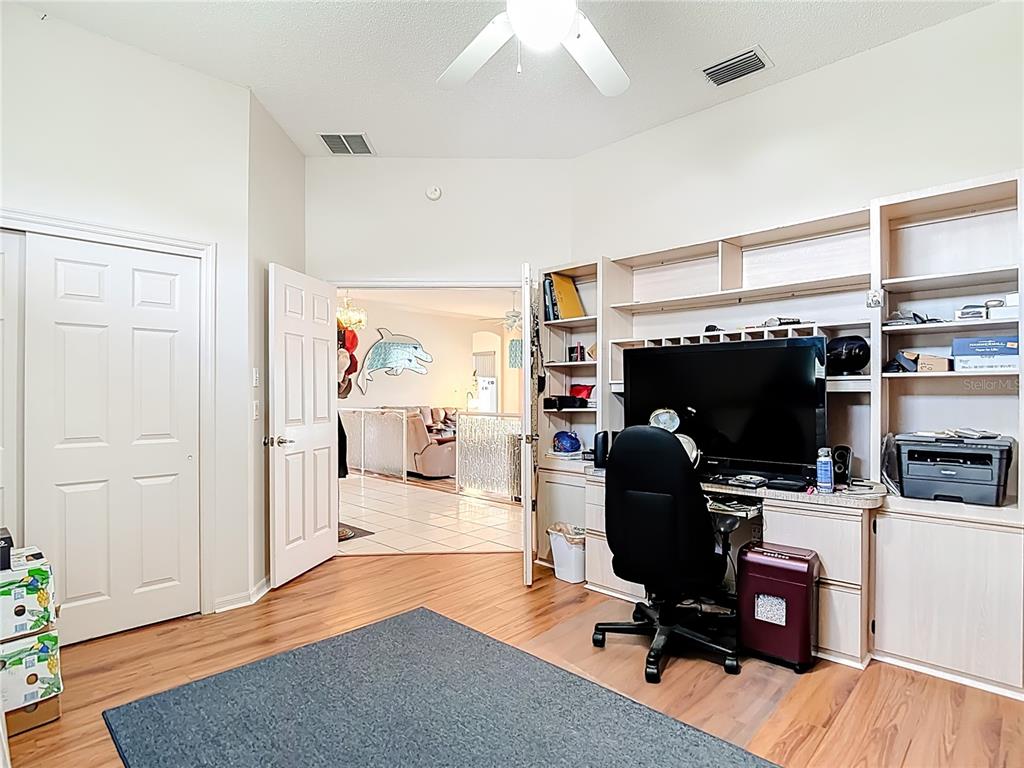 A home office features wood flooring, a built-in desk unit, and an open doorway to another room — 8410 MAYBELLE DRIVE, WEEKI WACHEE, FL