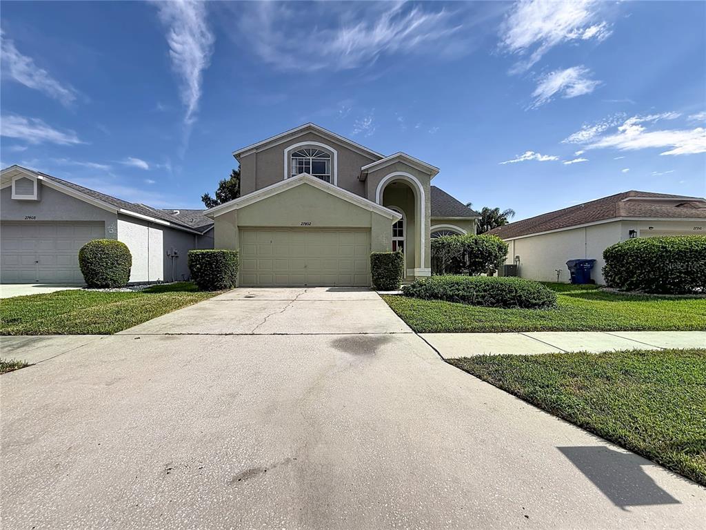 A two-story suburban house with a beige exterior, a two-car garage, and a concrete driveway — 27402 CORAL SPRINGS DRIVE, WESLEY CHAPEL, FL