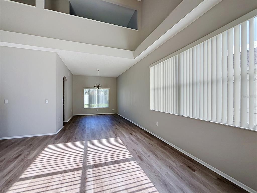 An empty dining area with wood-look flooring, high ceilings, and large windows with vertical blinds — 27402 CORAL SPRINGS DRIVE, WESLEY CHAPEL, FL