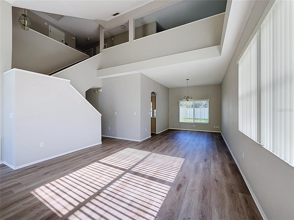 An open-concept living and dining area features light gray walls, wood-look flooring, and high ceilings — 27402 CORAL SPRINGS DRIVE, WESLEY CHAPEL, FL