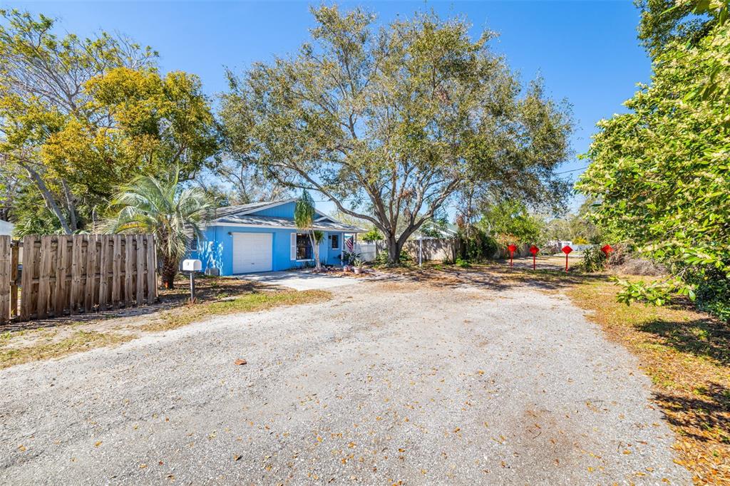A blue single-story house with a white garage door sits behind a large gravel driveway — 1335 15TH STREET, PALM HARBOR, FL
