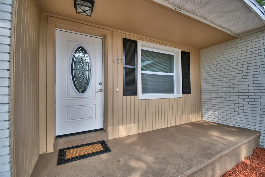 A white front door with an oval glass insert sits beside a window with black shutters — 1919 19TH STREET NW, WINTER HAVEN, FL