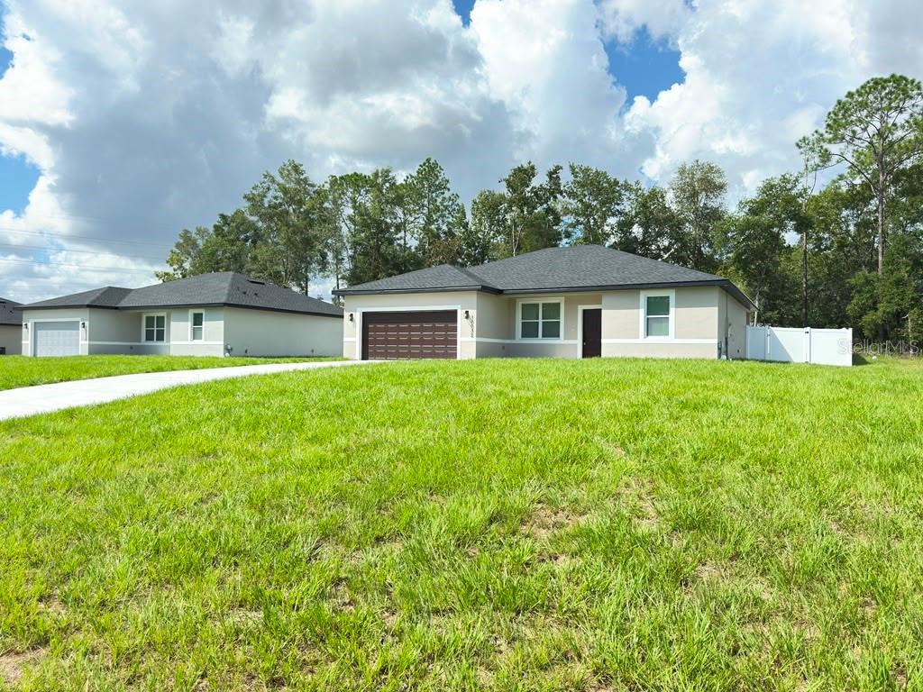 A view of two single-story suburban houses with driveways and lawns under a cloudy sky — 10032 N DELTONA BOULEVARD, DUNNELLON, FL
