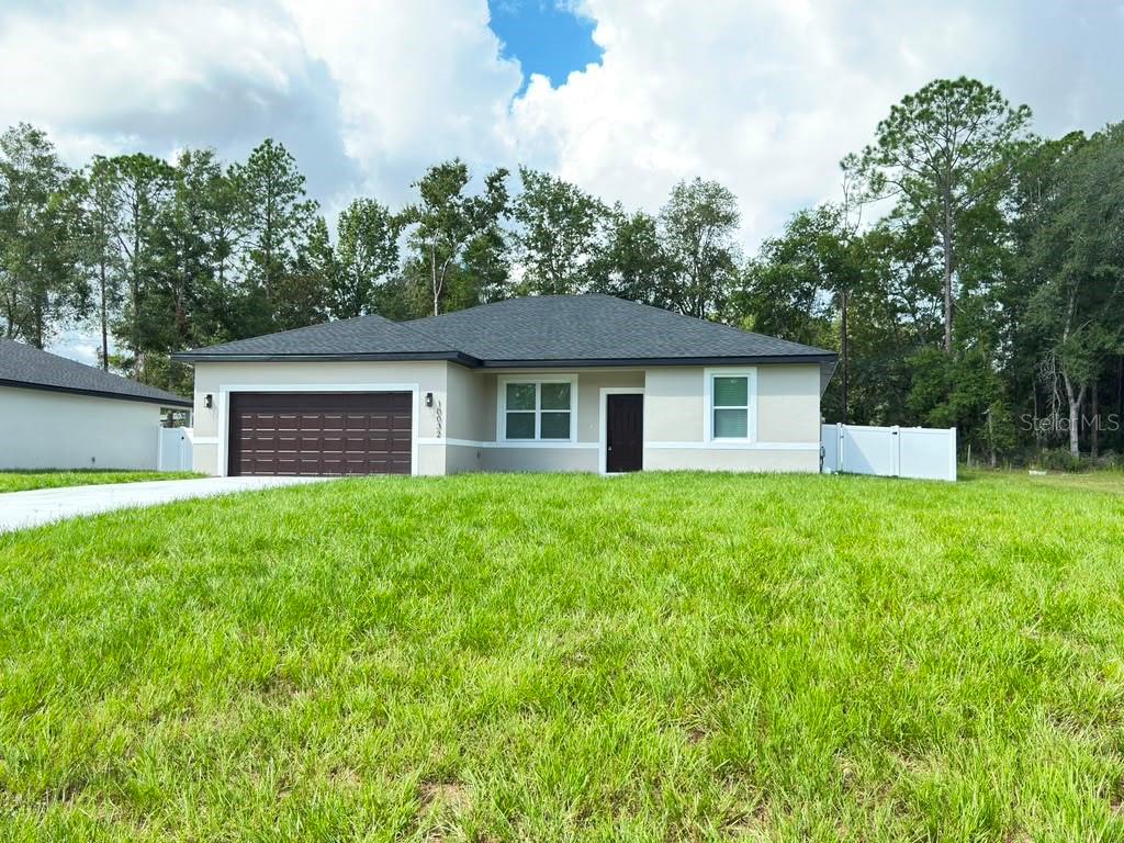 A single-story house with a brown garage door and white trim sits on a grassy lot — 10032 N DELTONA BOULEVARD, DUNNELLON, FL