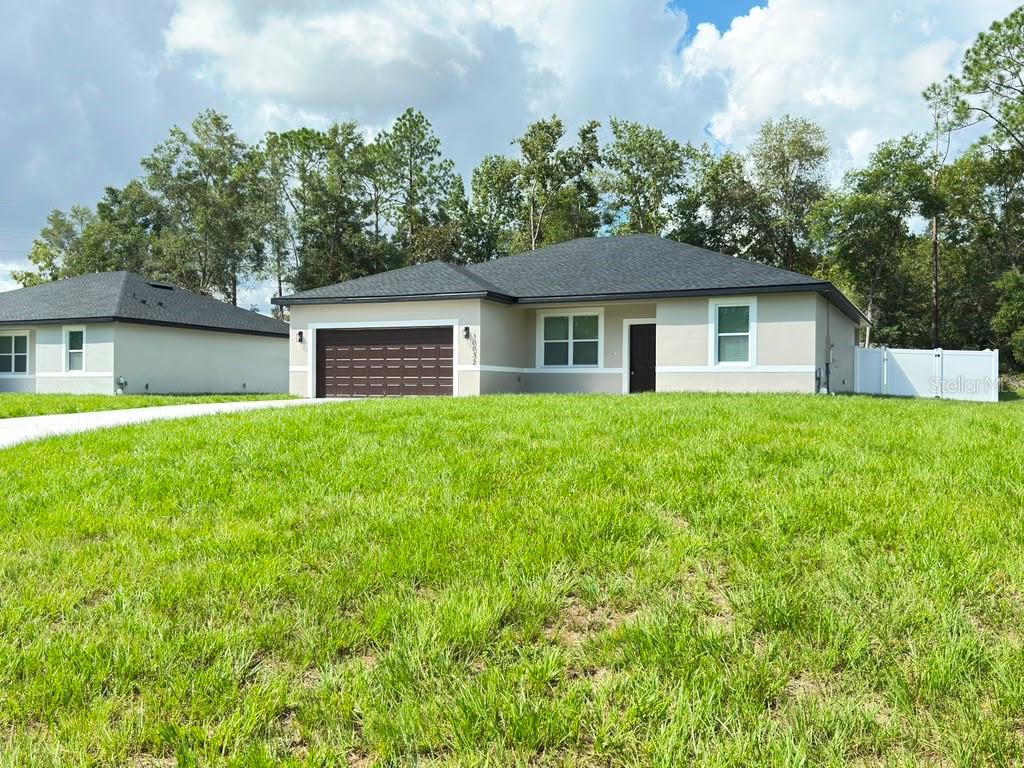A single-story house with a dark roof, tan stucco exterior, and a two-car garage — 10032 N DELTONA BOULEVARD, DUNNELLON, FL