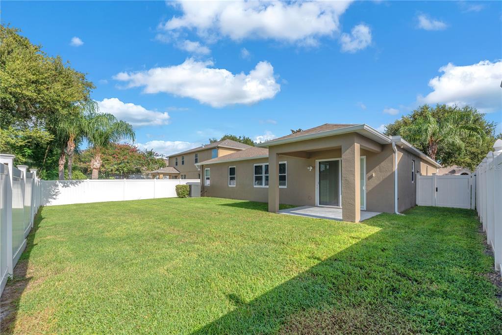 A backyard features a grassy lawn, a covered patio, and white vinyl privacy fencing — 1407 RUSHGROVE CIRCLE, DOVER, FL