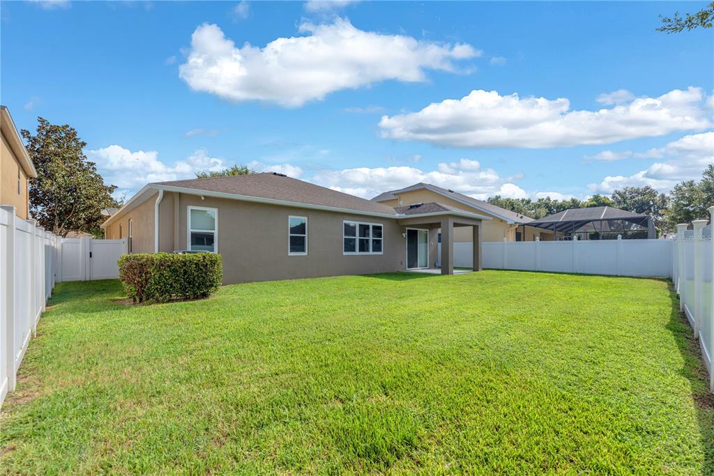 The backyard of a house features a tan exterior, a covered patio, and white fencing — 1407 RUSHGROVE CIRCLE, DOVER, FL