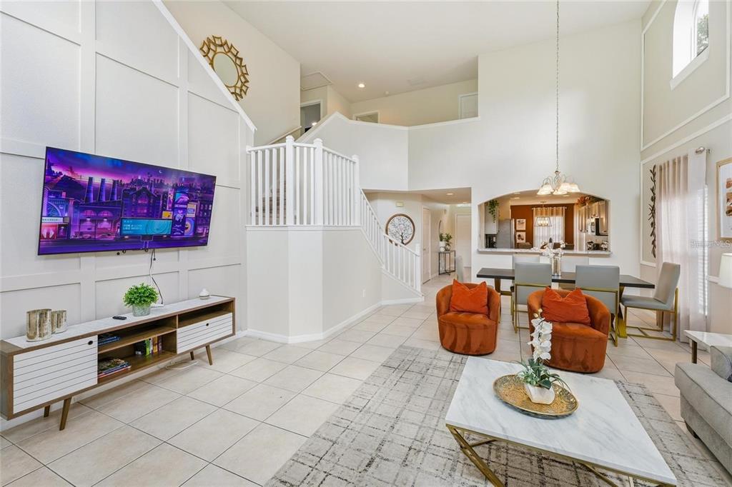 A bright living room features a mounted television, white paneled walls, and orange accent chairs — 8426 SECRET KEY COVE, KISSIMMEE, FL
