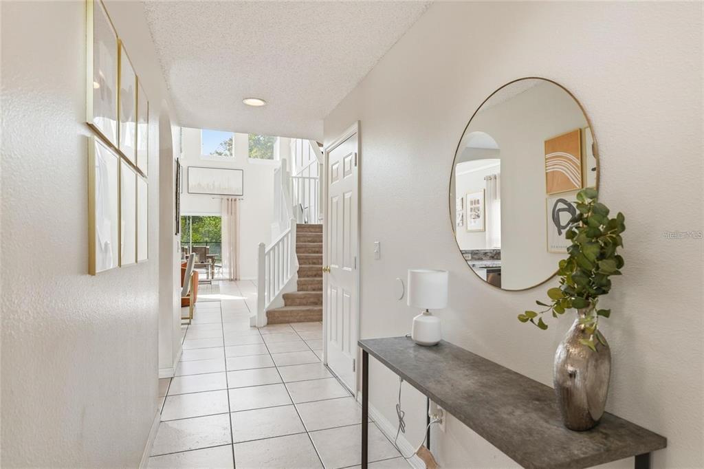 A tiled entryway features a console table, a round mirror, and stairs leading to a loft — 8426 SECRET KEY COVE, KISSIMMEE, FL