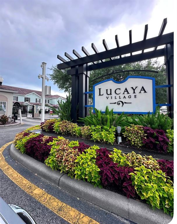 The entrance sign for Lucaya Village features a black pergola structure and landscaped garden beds — 5364 DIPLOMAT COURT UNIT 108, KISSIMMEE, FL