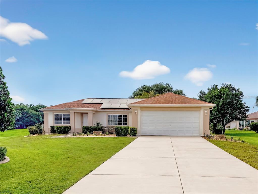 A single-story house with a white garage, tan exterior, and solar panels on the roof — 13520 SE 87TH CIRCLE, SUMMERFIELD, FL