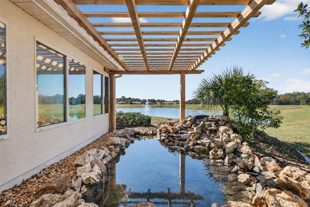 A wooden pergola covers a stone-lined pond next to a house overlooking a lake — 13520 SE 87TH CIRCLE, SUMMERFIELD, FL