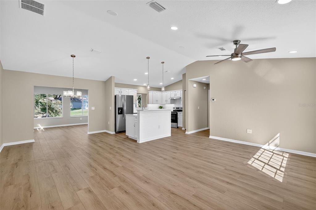 An open-concept living area features light wood-look flooring, a kitchen with white cabinets, and lighting — 13520 SE 87TH CIRCLE, SUMMERFIELD, FL